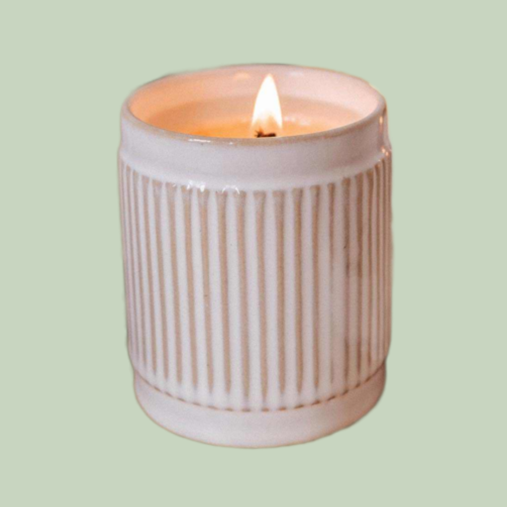 Ambre reusable soy candle in ribbed white ceramic container on sage green background.