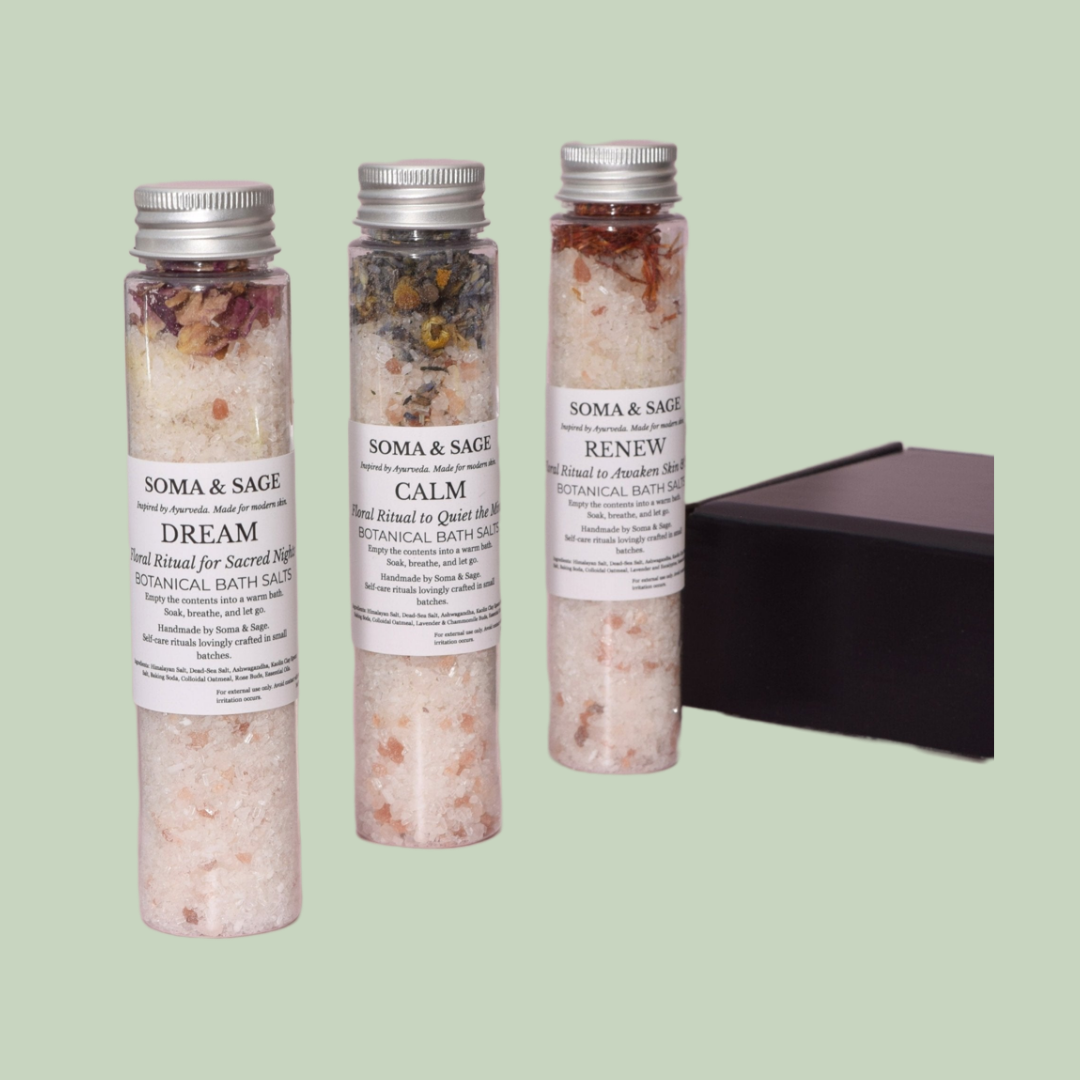 Three Soma & Sage bath salt tubes with silver caps, labelled Dream, Calm, Renew, beside a black gift box on a sage-green background.