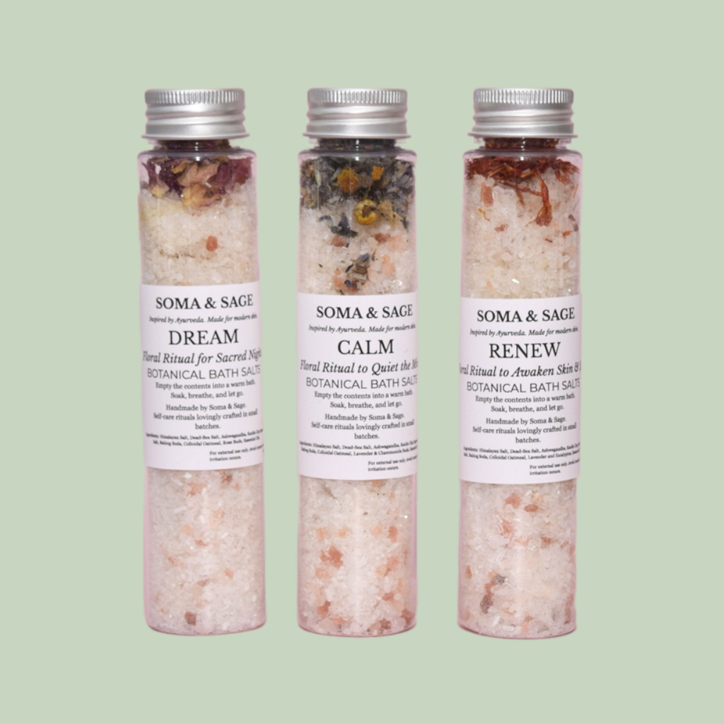 Three clear Soma & Sage botanical bath salt tubes with silver caps, labelled Dream, Calm, Renew, standing on a sage-green background.