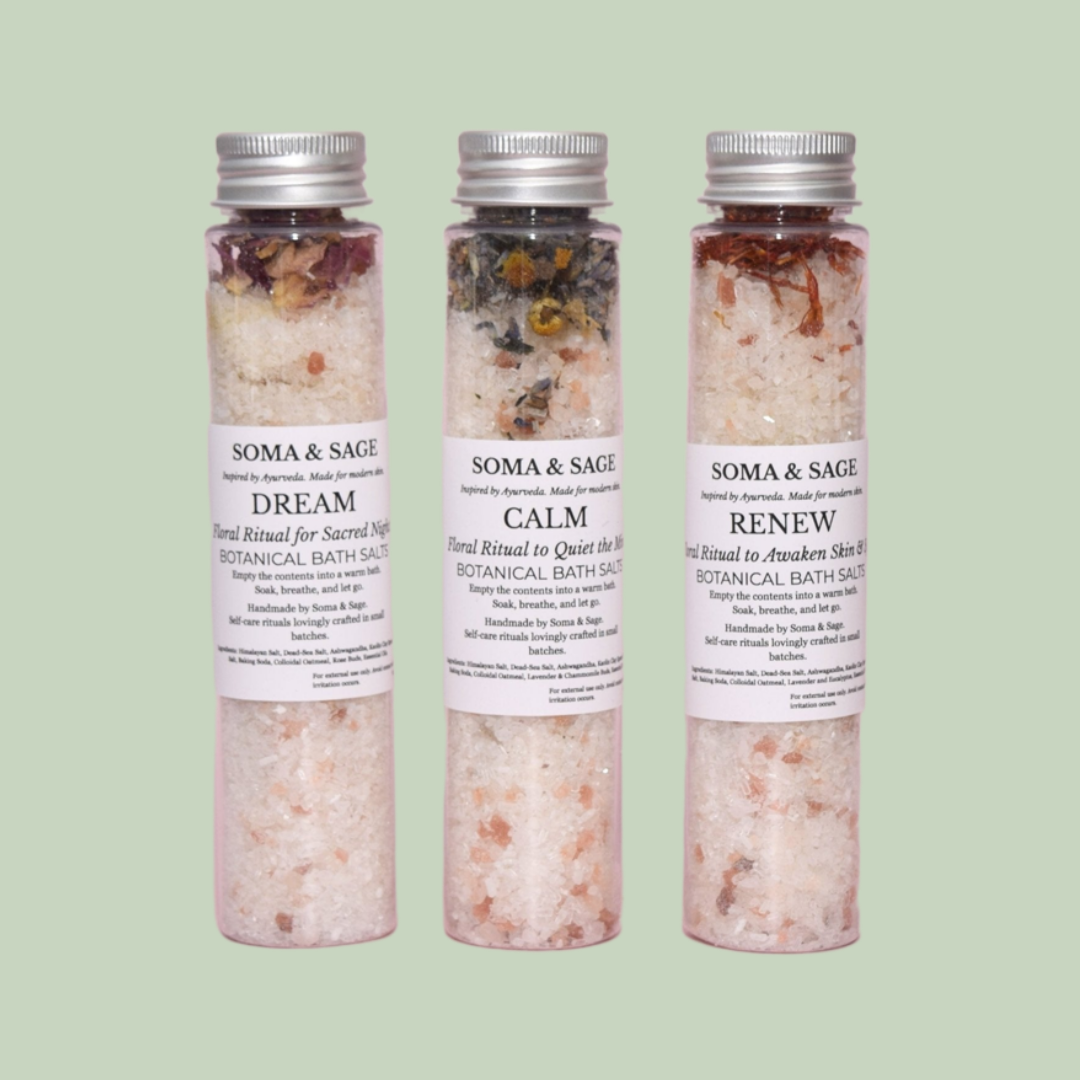 Three clear Soma & Sage botanical bath salt tubes with silver caps, labelled Dream, Calm, Renew, standing on a sage-green background.