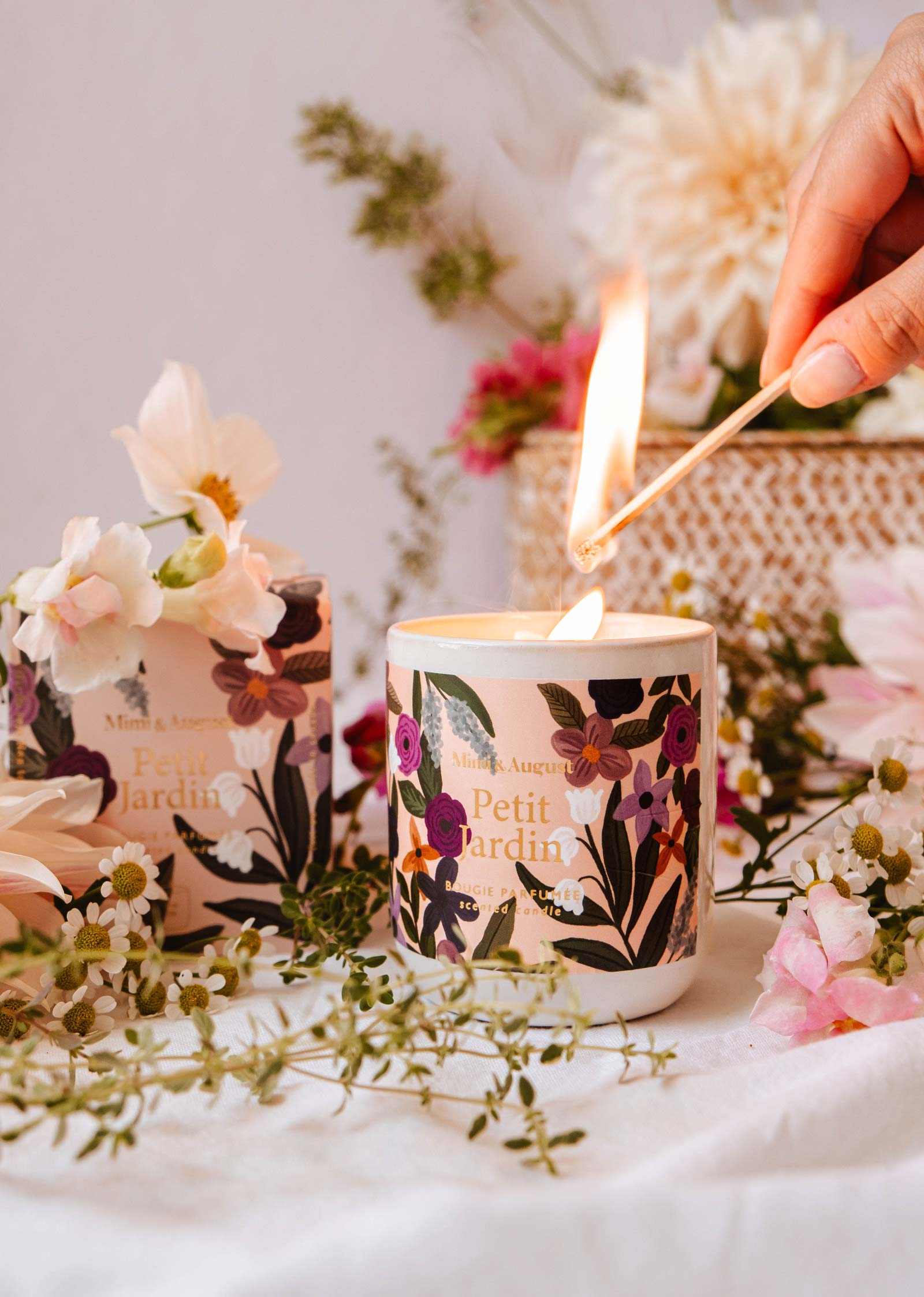 Hand lighting Petit Jardin botanical candle surrounded by fresh pink flowers — candle ritual — Sensory for Calm